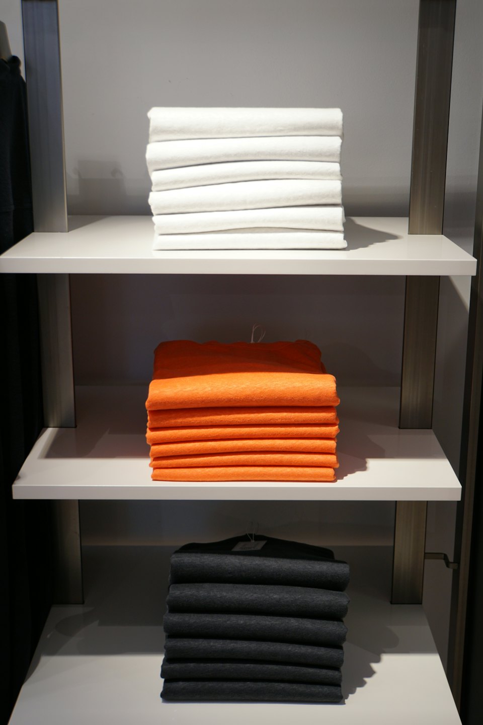 Ordentlich gefaltete T-Shirts in Weiß, Orange und Grau in einem Ladenregal.