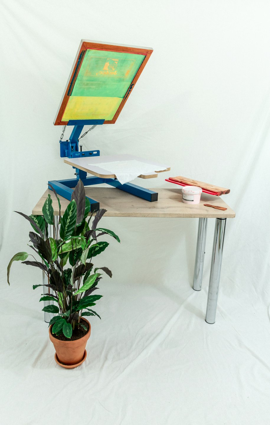 Siebdruckmaschine mit T-Shirt und Farbvorräten auf einem Tisch.