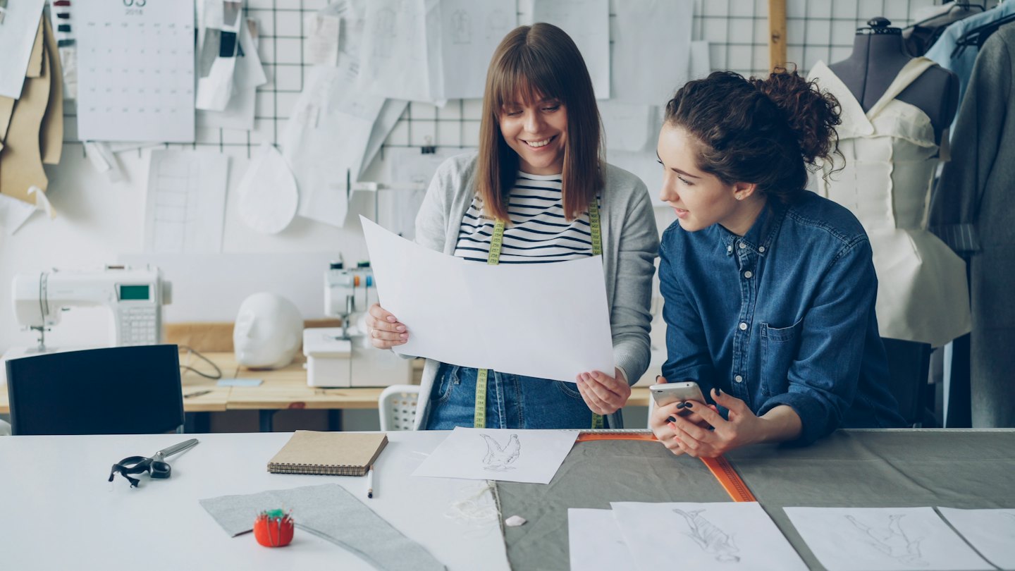 Zwei Frauen besprechen Modeentwürfe in einem Atelier.