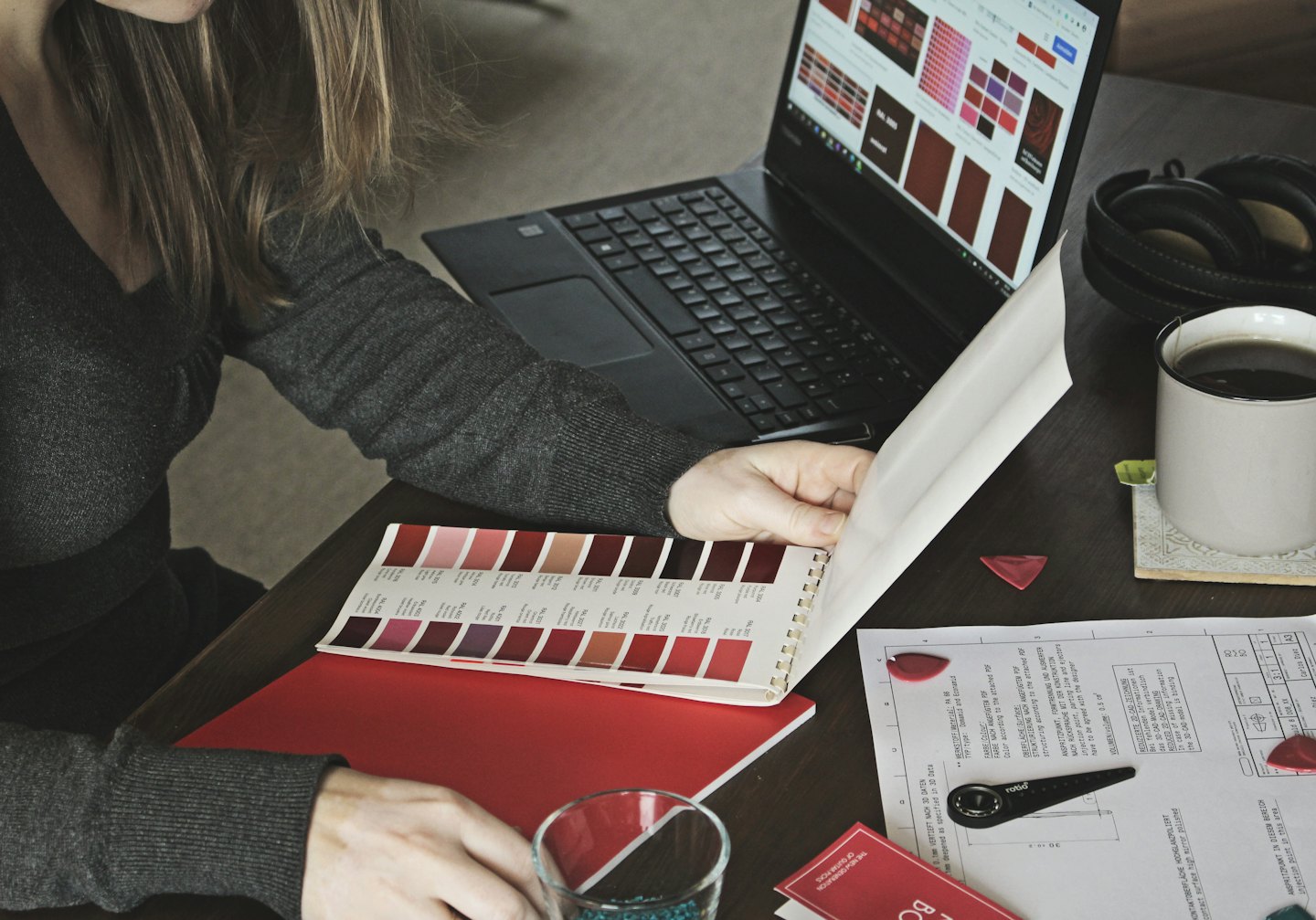 Designerin prüft Farbfelder auf einem Laptop und in einem Buch.
